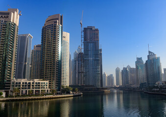 Obraz premium Dubai Marina skyline with modern skyscrapers and waterfront reflections under clear blue sky, luxury urban architecture in UAE.