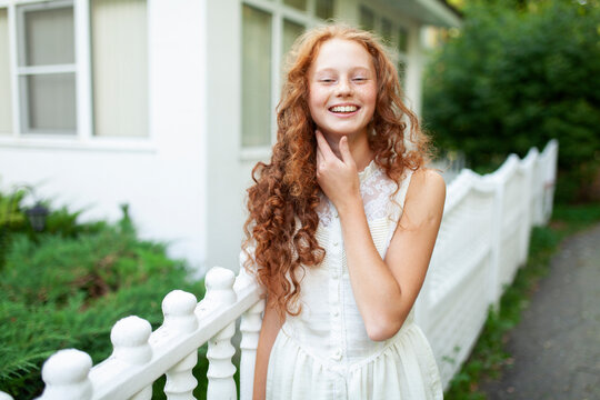 Smiling red haired teenager outdoors by white fence at home