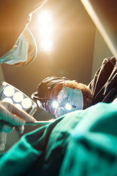 Surgeons In Operating Room Perform Delicate Procedure Under Bright Surgical Lights And Magnifying Loupes