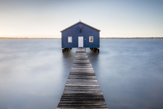 View of the iconic blue boat house stands serenely on stilts, connected by a weathered wooden jetty that stretches into the tranquil water, Perth, Western Australia, Australia.