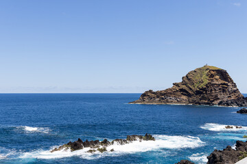 Basalt cliffs and offshore islet near Porto Moniz Madeira coast, powerful Atlantic waves strike layered volcanic rock creating dramatic textures against deep blue open water