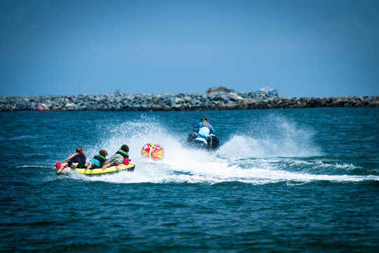 View of the aquamarine sea, where a vibrant yellow inflatable tube carrying three people is pulled by a jet ski, creating splashes, Lagos, Lagos, Nigeria.