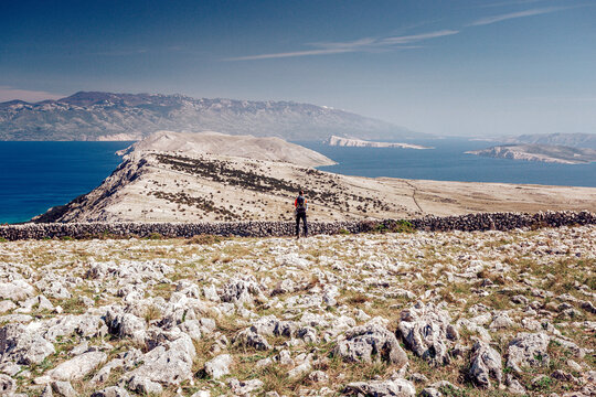 View of a lone figure stands atop a rocky hill overlooking the azure sea and distant islands under a clear sky, Ba&Aring;&iexcl;ka, Primorje-Gorski Kotar County, Croatia.
