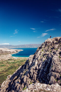 View of a lone figure stands atop a craggy peak overlooking the azure sea and distant shore, under a bright blue sky, Ba&Aring;&iexcl;ka, Primorje-Gorski Kotar County, Croatia.