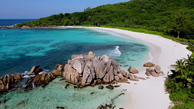 Experience the serene beauty of Anse Cocos beach on La Digue Island, Seychelles. Crystal clear waters gently lap against the shore, showcasing vibrant rocks and lush greenery in the background.