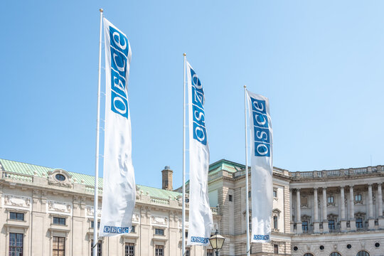 White OSCE flags waving in front of historic Hofburg complex in Vienna during clear weather.