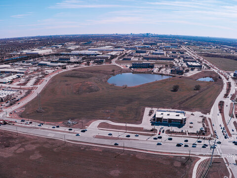 Aerial view of a serene pond reflecting the sky amidst a sprawling cityscape under a blanket of hazy light, Dallas, Texas, United States.