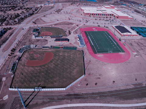 Aerial view of sports fields and a school building under a blue sky, with a baseball field, football field, and running track, Dallas, Texas, United States.