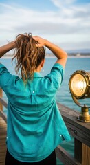 Fototapeta premium Young caucasian female with ponytail in turquoise shirt enjoying scenic ocean view on wooden pier during sunset