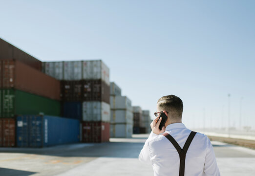 Rear view of manager talking on cell phone in front of cargo containers on industrial site