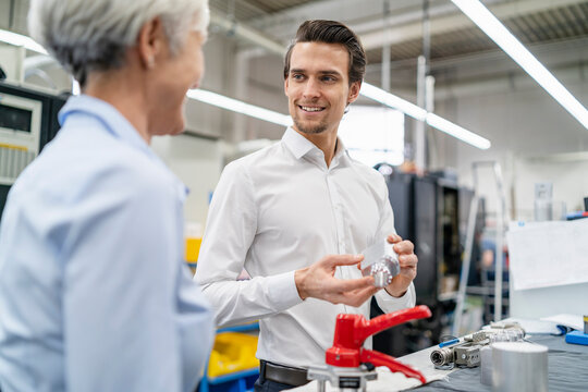 Smiling businessman and senior businesswoman with workpiece in a factory