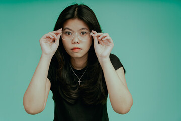 Omg! It is season of discouts! Beautiful and funny face expression of young asian lady touching her spectacles isolated on tosca green background.