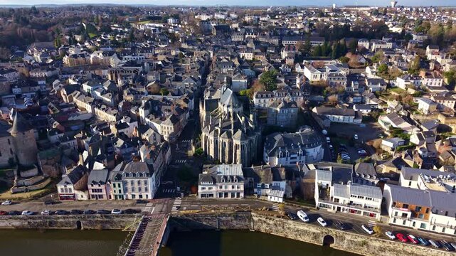 Basilica of Notre Dame of Miracles, bridge, and the Mayenne river in historic town of Mayenne, France. Aerial drone forward