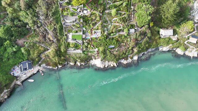 Aerial drone footage showing turquoise coastal waters, rocky shoreline, and seaside houses in Salcombe, Devon, England on a calm day.