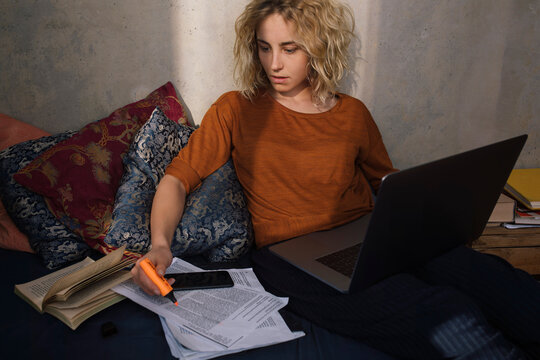 Portrait of blond student sitting with laptop on bed working