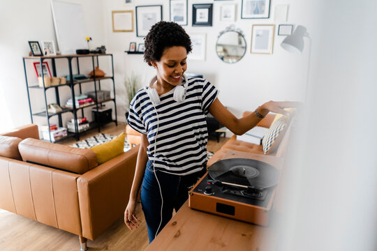 Young woman using record player at home