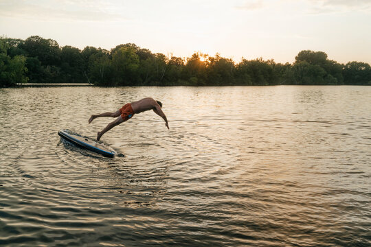 Man jumping from SUP board on a lake at sunset