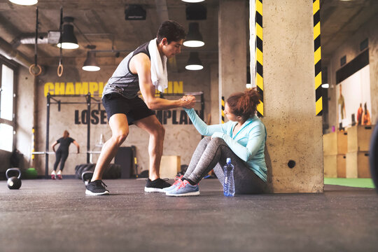 Athlete helping young woman getting up after a break in gym
