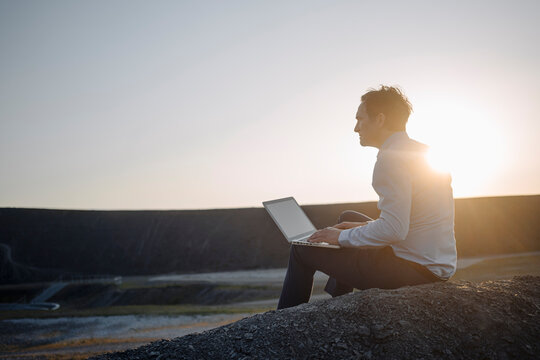 Mature businessman using laptop on a disused mine tip at sunset
