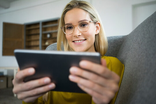 Portrait of smiling woman with glasses sitting on couch using mini tablet