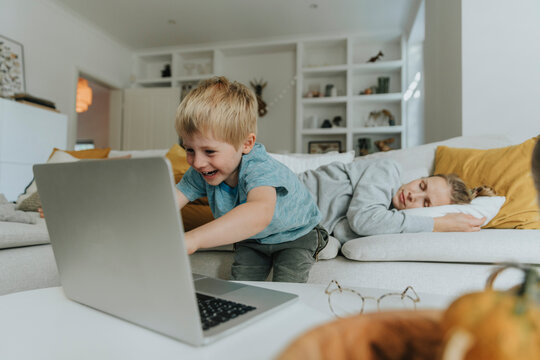 Boy using laptop by mother sleeping on sofa at home