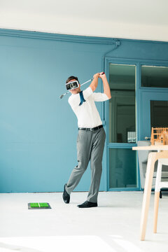 Businessman wearing VR glasses playing golf in office