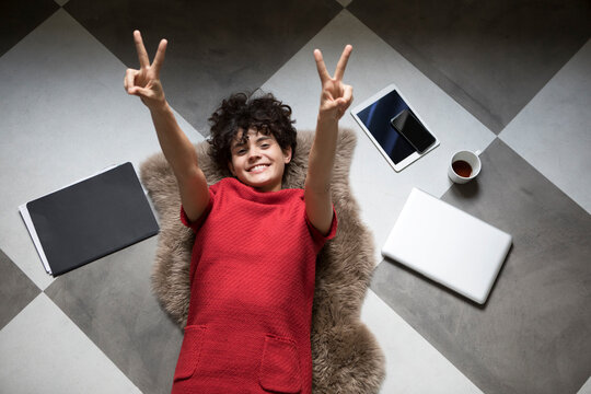 Portrait of happy young woman lying on the floor at home showing victory signs