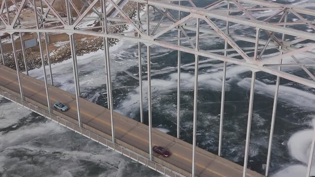 Cinematic drone footage of winter transportation infrastructure in Dubuque, Iowa showing a bridge, moving vehicles, and frozen river conditions. Suitable for commercial, travel, and editorial projects
