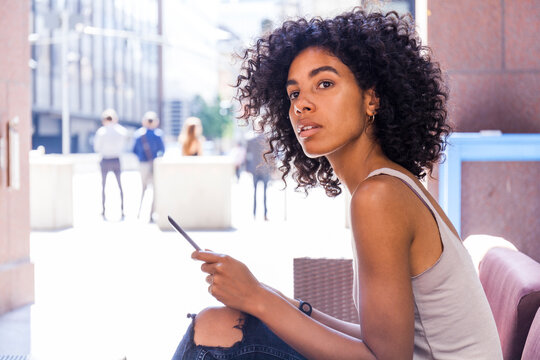 Portrait of young woman with digital tablet sitting at sidewalk cafe watching something