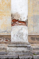 A close-up of a weathered classical column with cracked white plaster revealing exposed red brick, worn stone base and textured facade conveying age, decay, architectural detail and historic charm