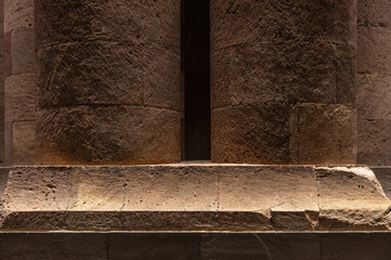 Warm-lit ancient stone columns and a massive column base showcase weathered masonry and textured stonework in a historic temple or ruin, evoking timelessness, strength and architectural heritage