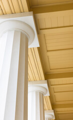 Sunlit columned arcade with tall white pillars and crown molding creates a timeless, grand atmosphere. The warm yellow ceiling adds depth and elegance to a stately architectural setting