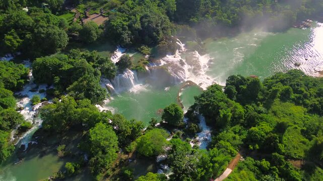 Stunning drone footage of Ban Gioc Detian Falls, showing multiple tiers of cascading water surrounded by lush tropical vegetation and turquoise pools in Cao Bang