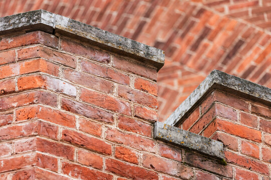 A detailed close-up of red brick walls featuring aged mortar, weathered stone caps, and layered parapet edges, capturing historic architectural textures and the rustic charm of brick construction
