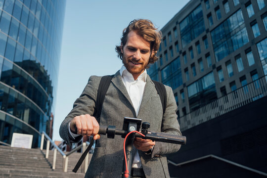 Male entrepreneur using mobile phone while standing with electric push scooter at downtown