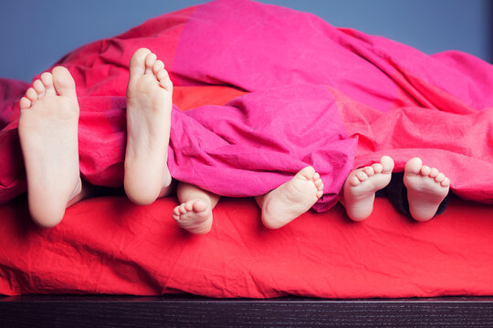 Feet of three siblings lying side by side in bed