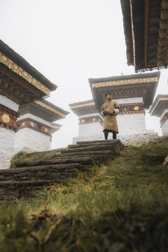 View of a serene figure standing amidst the ancient stupas, their white walls and golden roofs piercing the misty air, Dochula Chorten, Thimphu, Bhutan.
