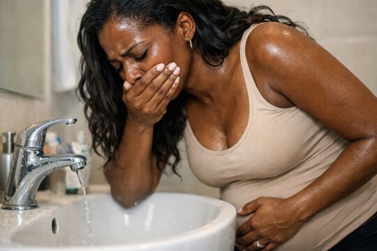 Pregnant African American woman suffering from strong morning sickness and nausea in bathroom. Concept of early pregnancy toxicosis and health problems.