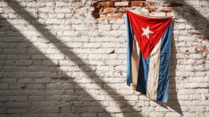 Cuban flag hangs on a brick wall with sunlight casting shadows in an urban setting