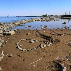 Sandcastle with stone fence on bay shoreline against industrial backdrop &mdash; ideal for environmental contrast, childhood resilience and urban nature documentation.