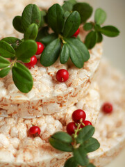 Close-up of rice cakes topped with lingonberry sprigs (Vaccinium vitis-idaea). Red berries and green leaves create a natural accent for a healthy snack concept.