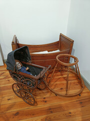 Vintage baby carriage with porcelain doll, antique wooden cradle and rocking stand in historical interior. Old childhood and retro family life concept.