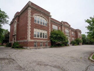 Obraz premium Historic red brick school building standing stately under an overcast sky, evoking a dreamlike nostalgia and past memories