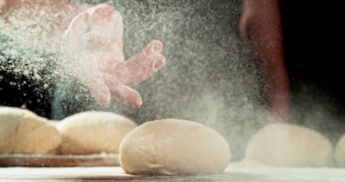 Super slow motion, 1000 fps close-up of baker&rsquo;s hand tossing flour over prepared risen dough on wooden table. Cinematic baking concept, artisan bread preparation and texture detail. Speed ramp effect.