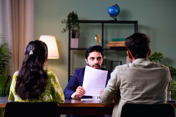 Young Indian husband and wife analyzing financial reports with planner in office