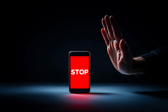 Digital detox concept with a smartphone showing STOP on screen while a hand gesture signals warning and control. A dark studio scene about addiction and healthier boundaries.