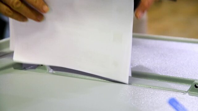 Close-up of a man's hands dropping sheets of paper or a ballot into a voting machine.