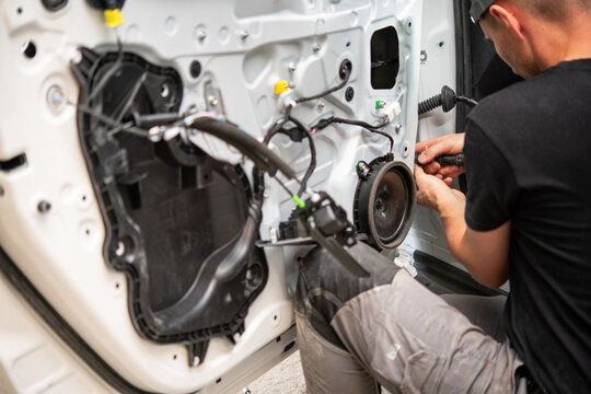 Man repairing car door wiring and speaker inside body shop