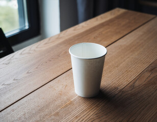White paper cup mockup on a wooden table in a bright interior