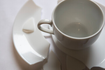 Broken cup and plate sit on a flat surface after an accident in a kitchen, creating a mess and needing cleanup